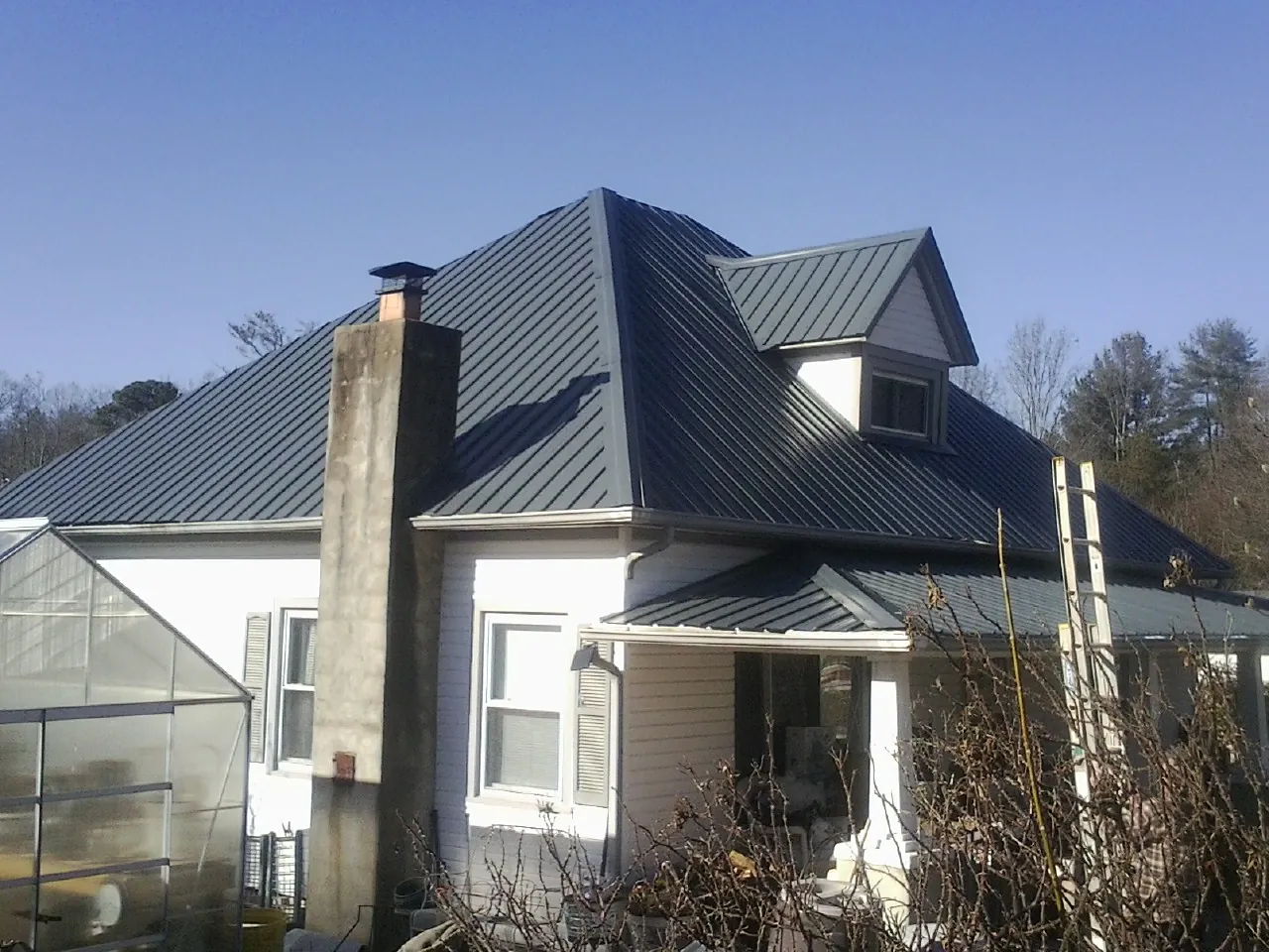 Dark blue standing seam metal roof on a white farmhouse with dormer — Slate & Tile Roof Repair by Roofing Brothers in West Glacier