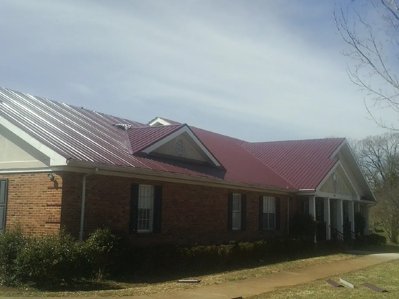 Red metal roof with gabled entries on a long brick building, from a Hail Damage Roof Repair job in West Glacier