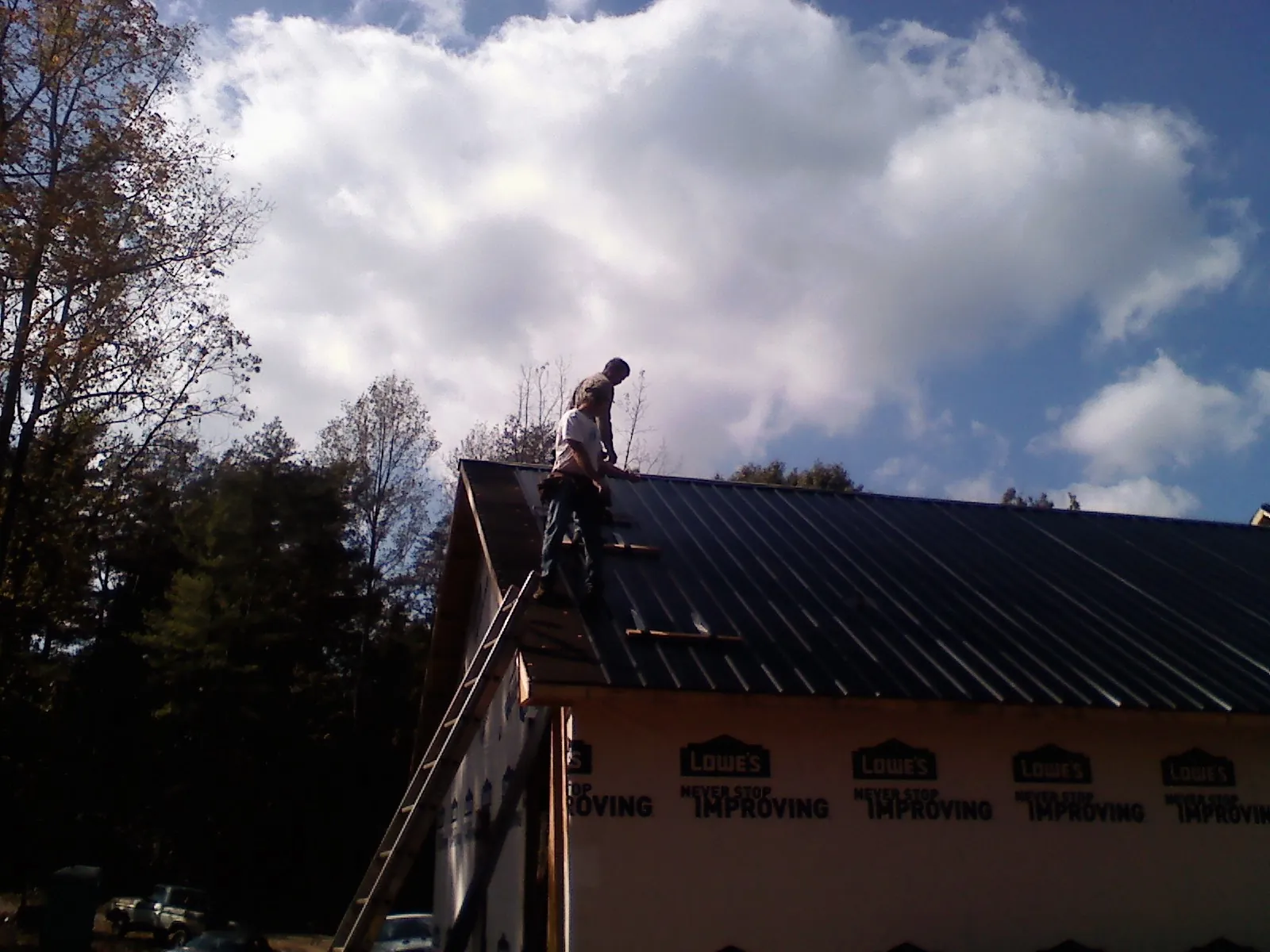 Roofer fastening dark metal panels high against a cloudy sky, from a Roof Inspection job in West Glacier