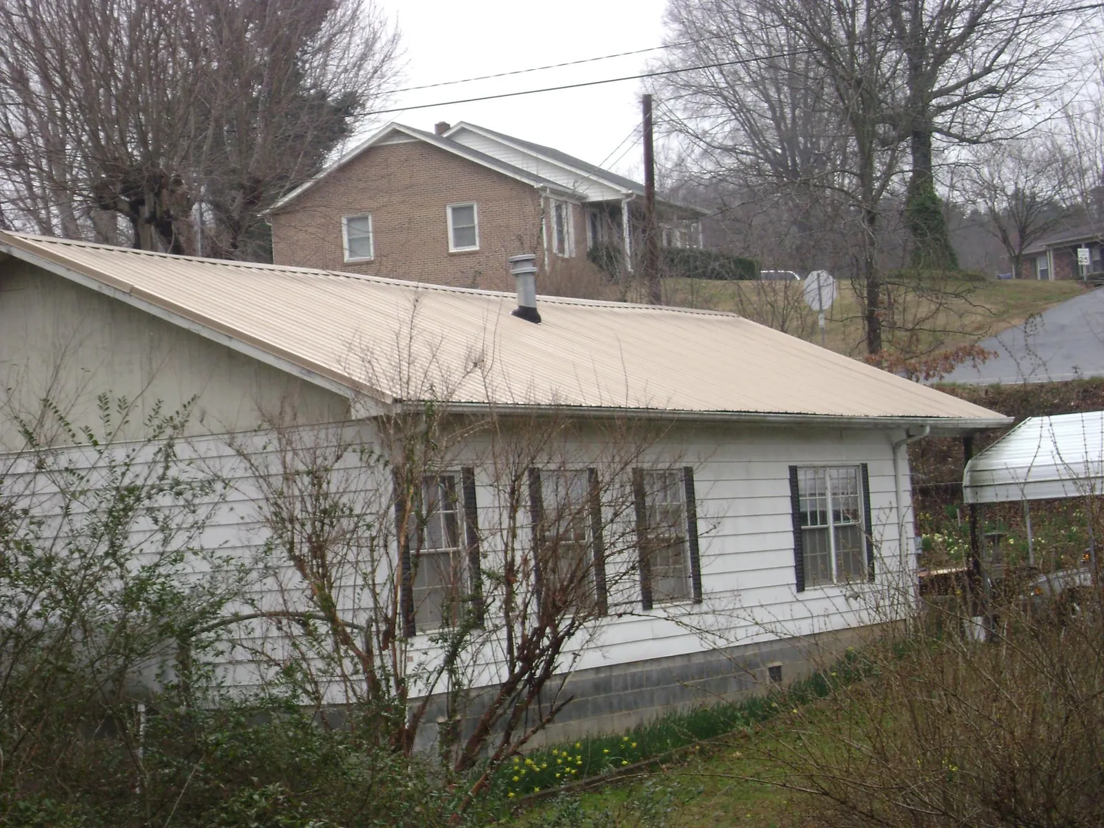 Tan metal roof on a white sided house set into a hillside — Commercial Roofing by Roofing Brothers in West Glacier